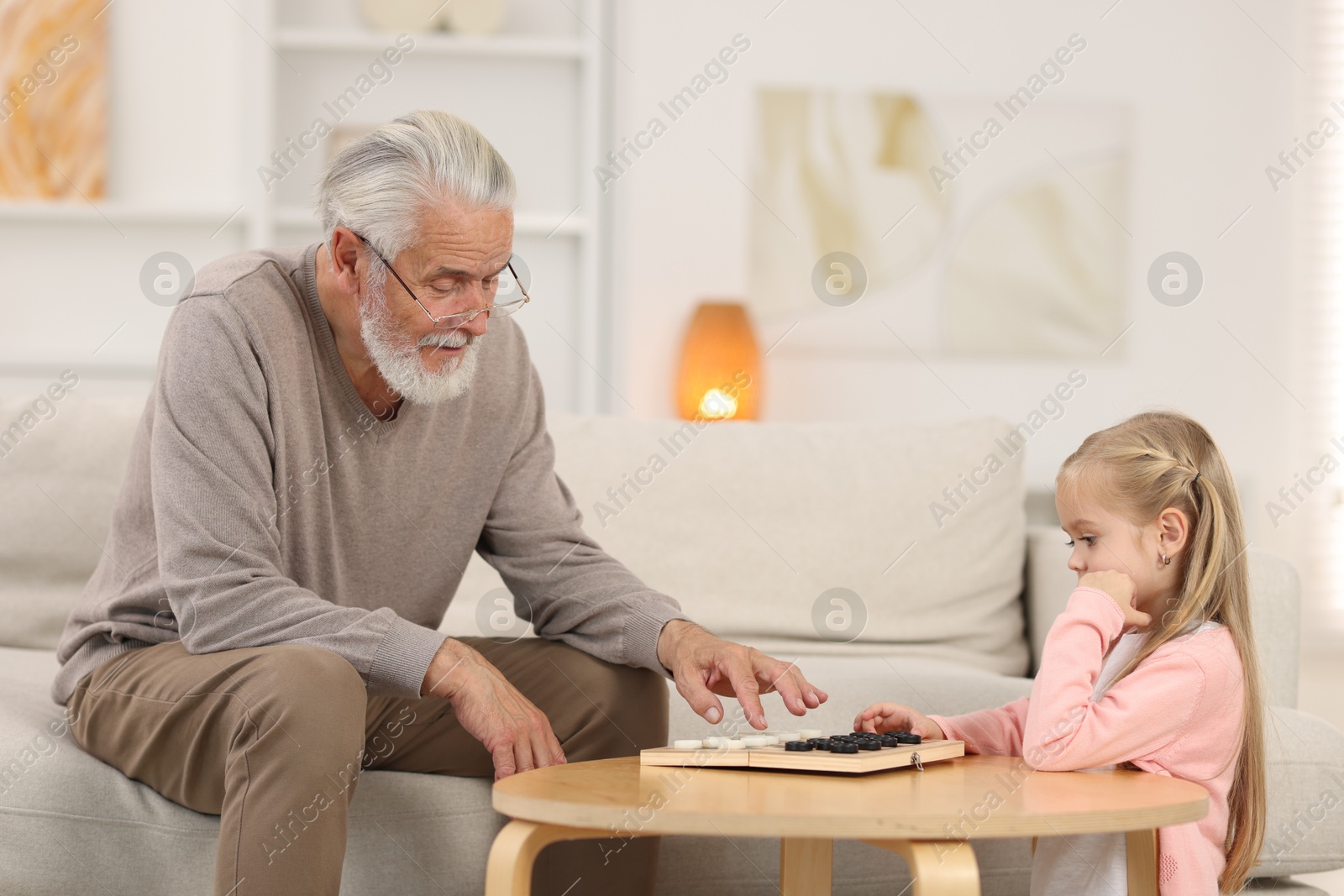 Photo of Grandpa and his granddaughter playing checkers at table indoors