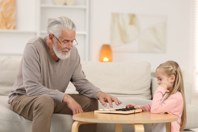 Photo of Grandpa and his granddaughter playing checkers at table indoors