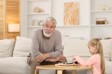 Photo of Grandpa and his granddaughter playing checkers at table indoors