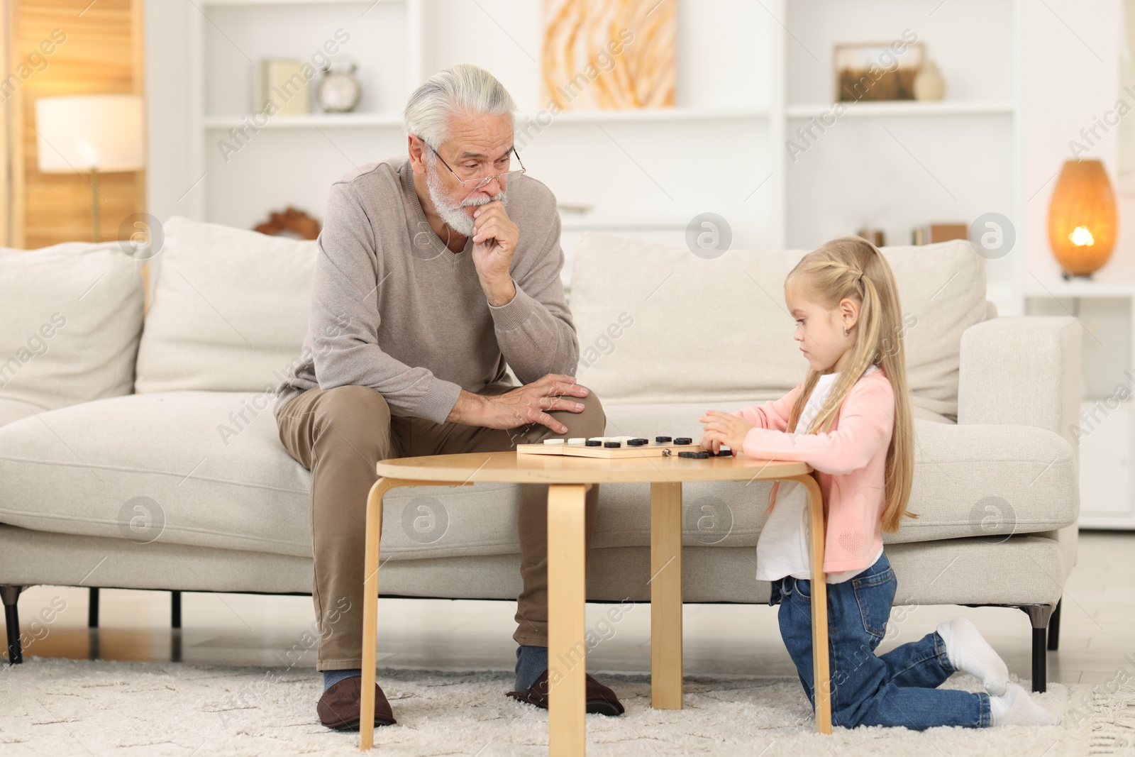 Photo of Grandpa and his granddaughter playing checkers at table indoors