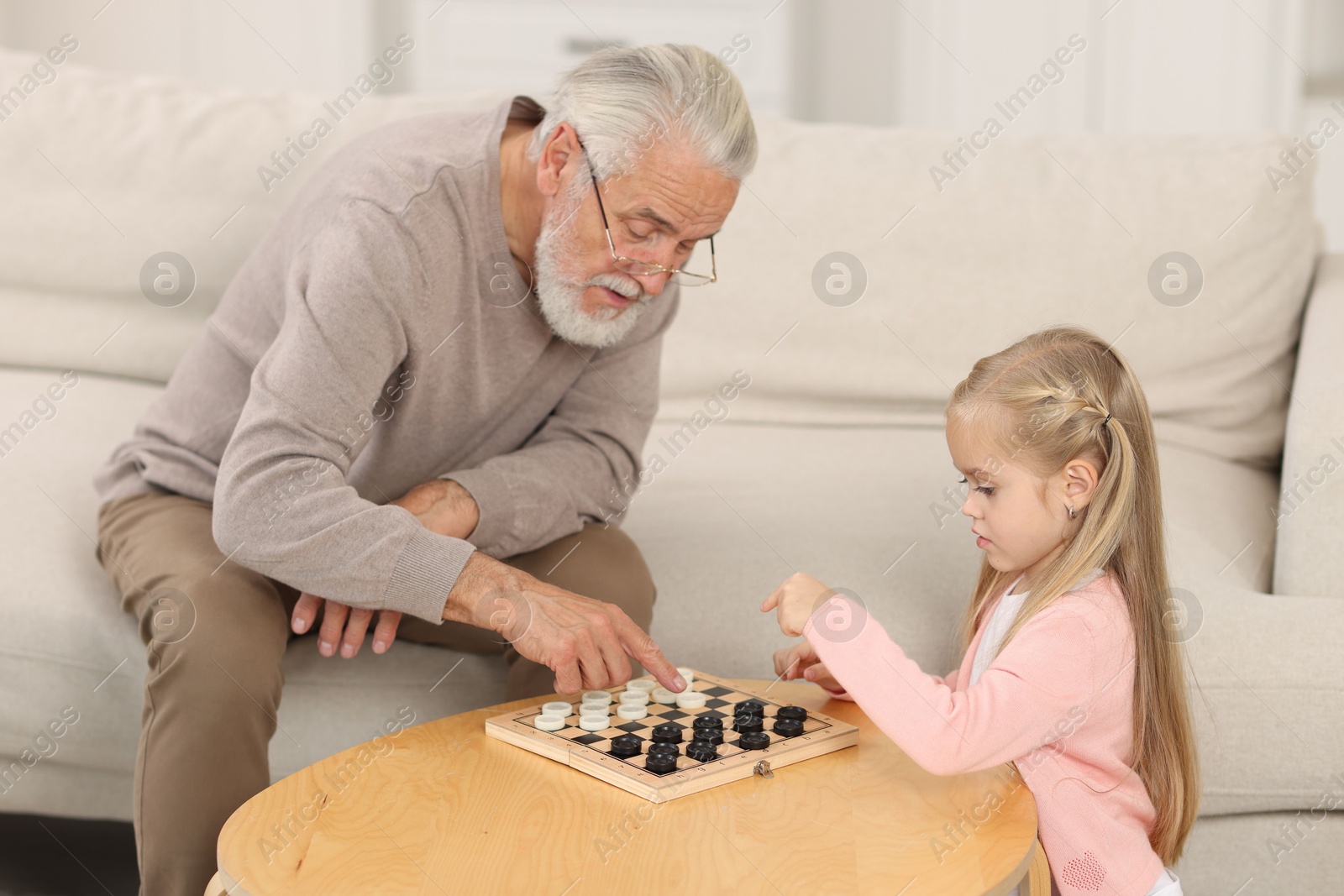 Photo of Grandpa and his granddaughter playing checkers at table indoors