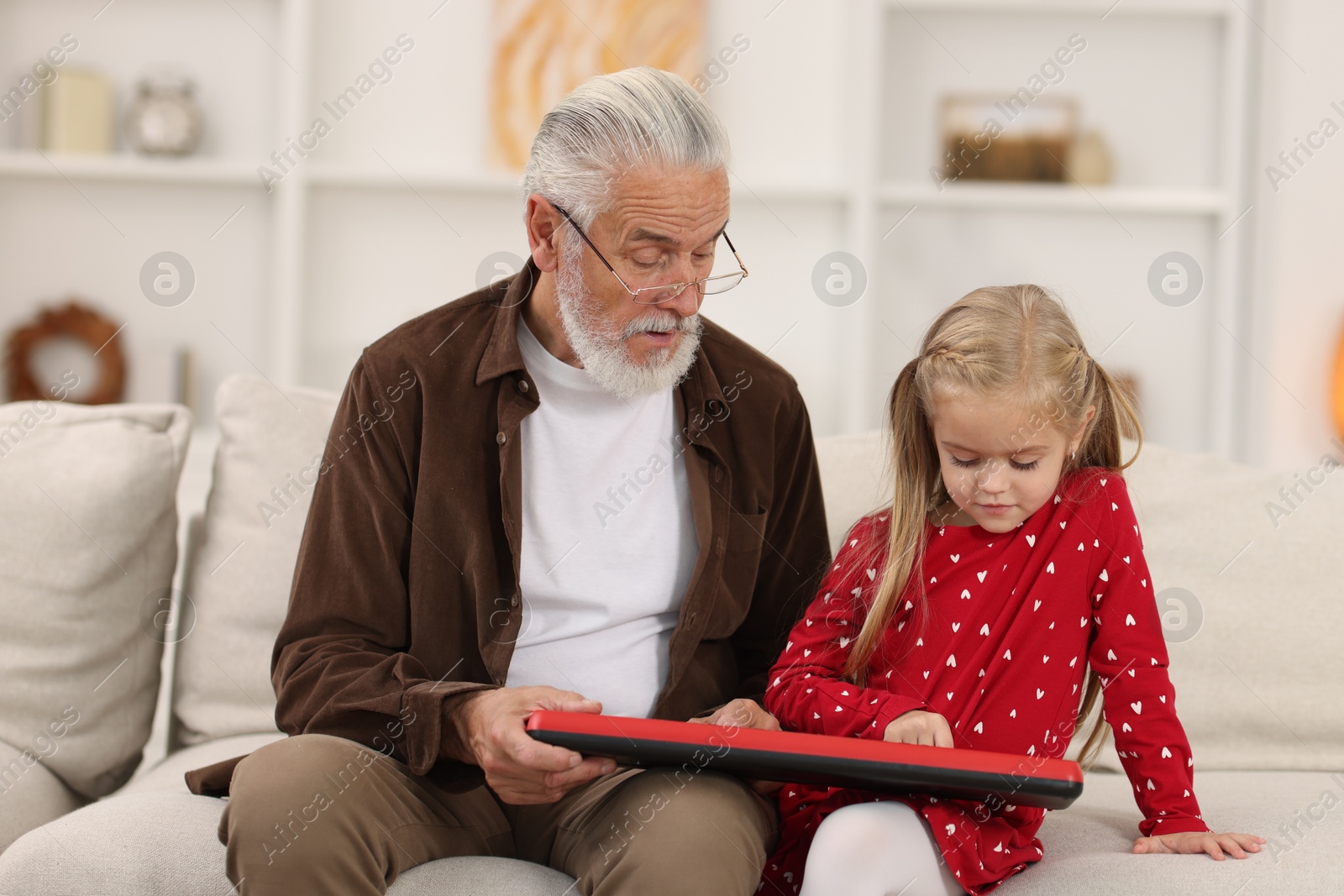 Photo of Grandpa and his granddaughter playing toy piano on sofa at home