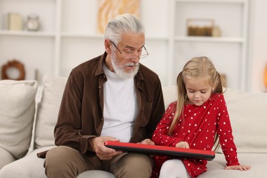 Grandpa and his granddaughter playing toy piano on sofa at home