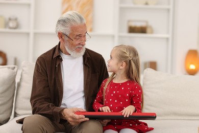 Grandpa and his granddaughter playing toy piano on sofa at home