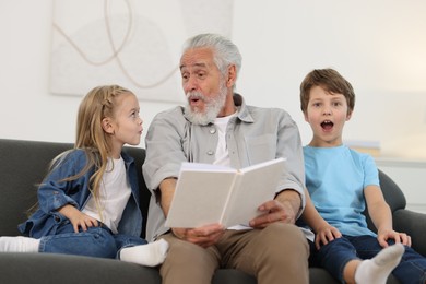 Grandpa and his grandkids reading book together on sofa at home