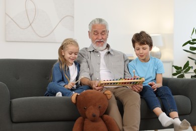 Grandpa and his grandkids playing toy xylophone on sofa at home