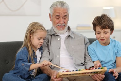 Photo of Grandpa and his grandkids playing toy xylophone on sofa at home