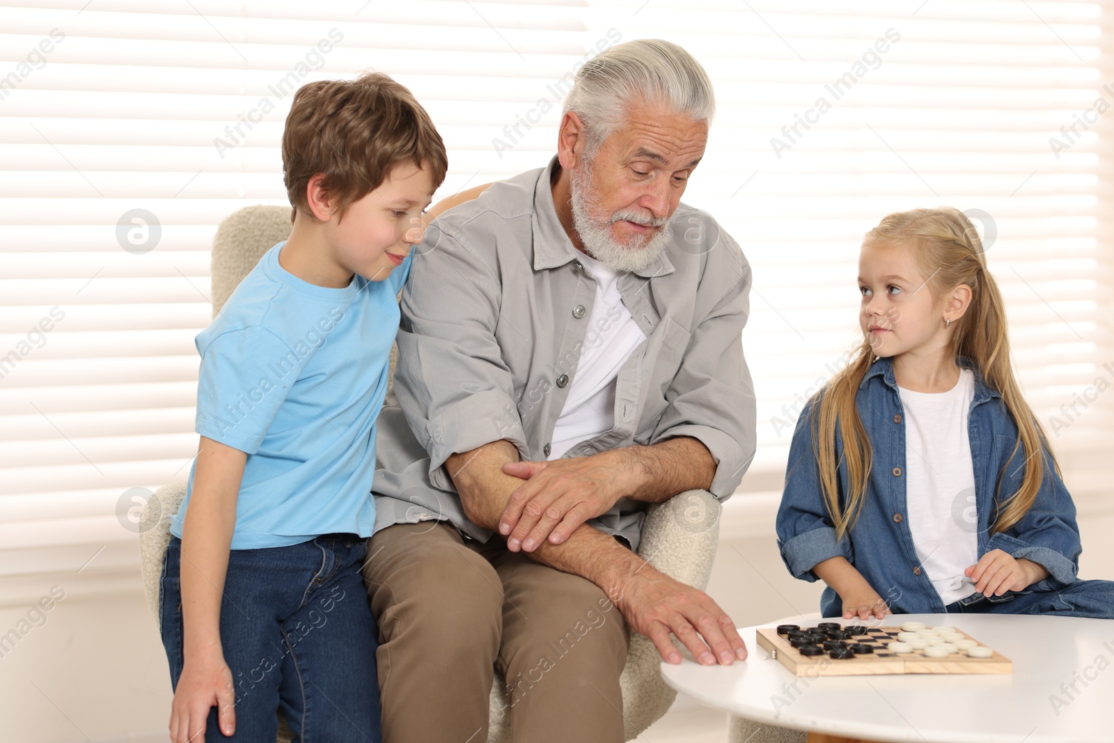 Photo of Grandpa and his grandkids playing checkers at table indoors