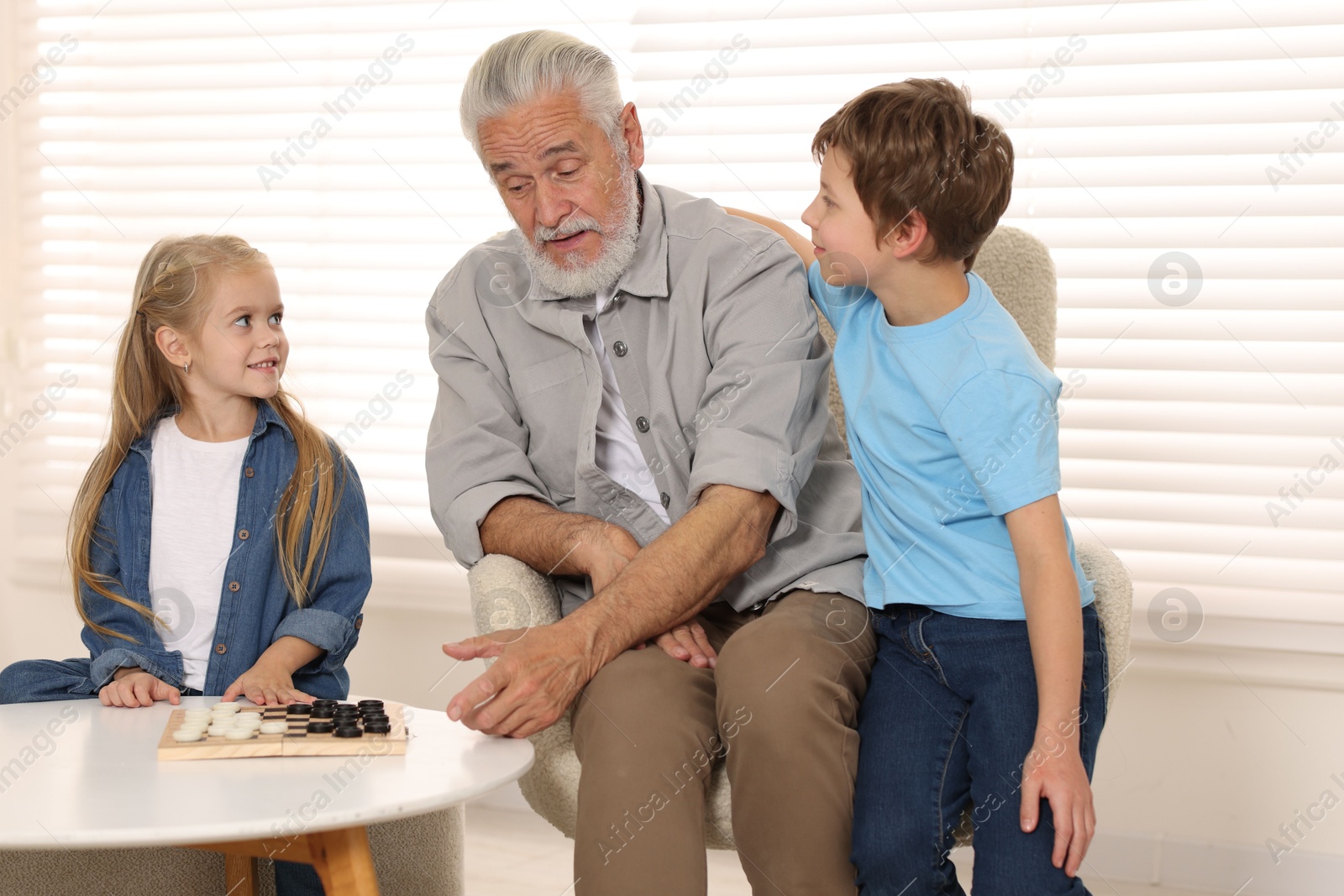 Photo of Grandpa and his grandkids playing checkers at table indoors