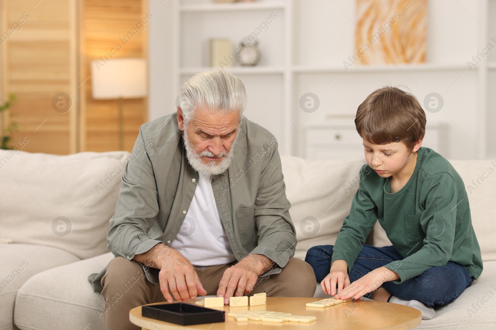 Photo of Grandpa and his grandson playing dominoes at table indoors