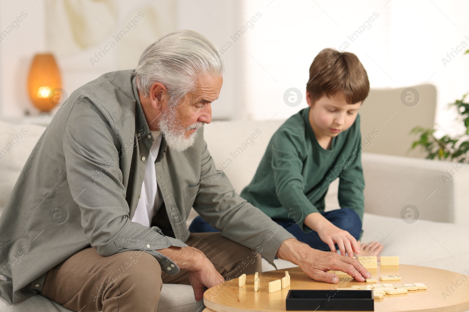 Photo of Grandpa and his grandson playing dominoes at table indoors