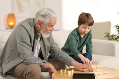 Photo of Grandpa and his grandson playing dominoes at table indoors