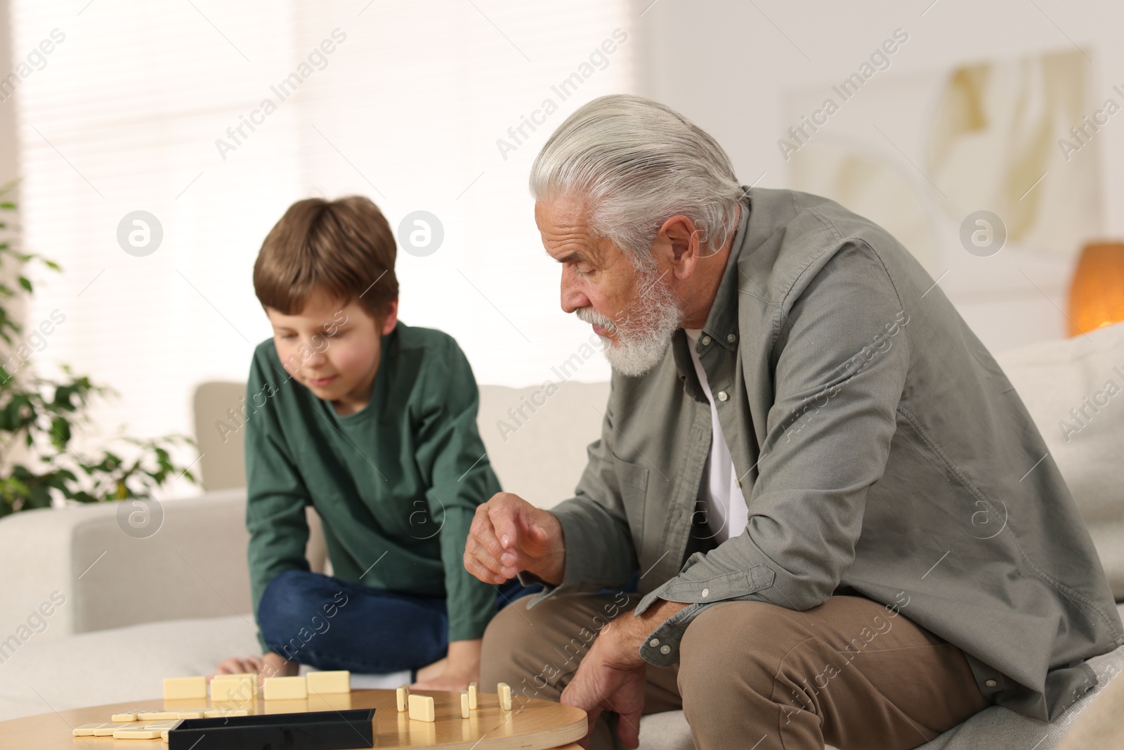 Photo of Grandpa and his grandson playing dominoes at table indoors