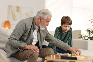 Photo of Grandpa and his grandson playing dominoes at table indoors