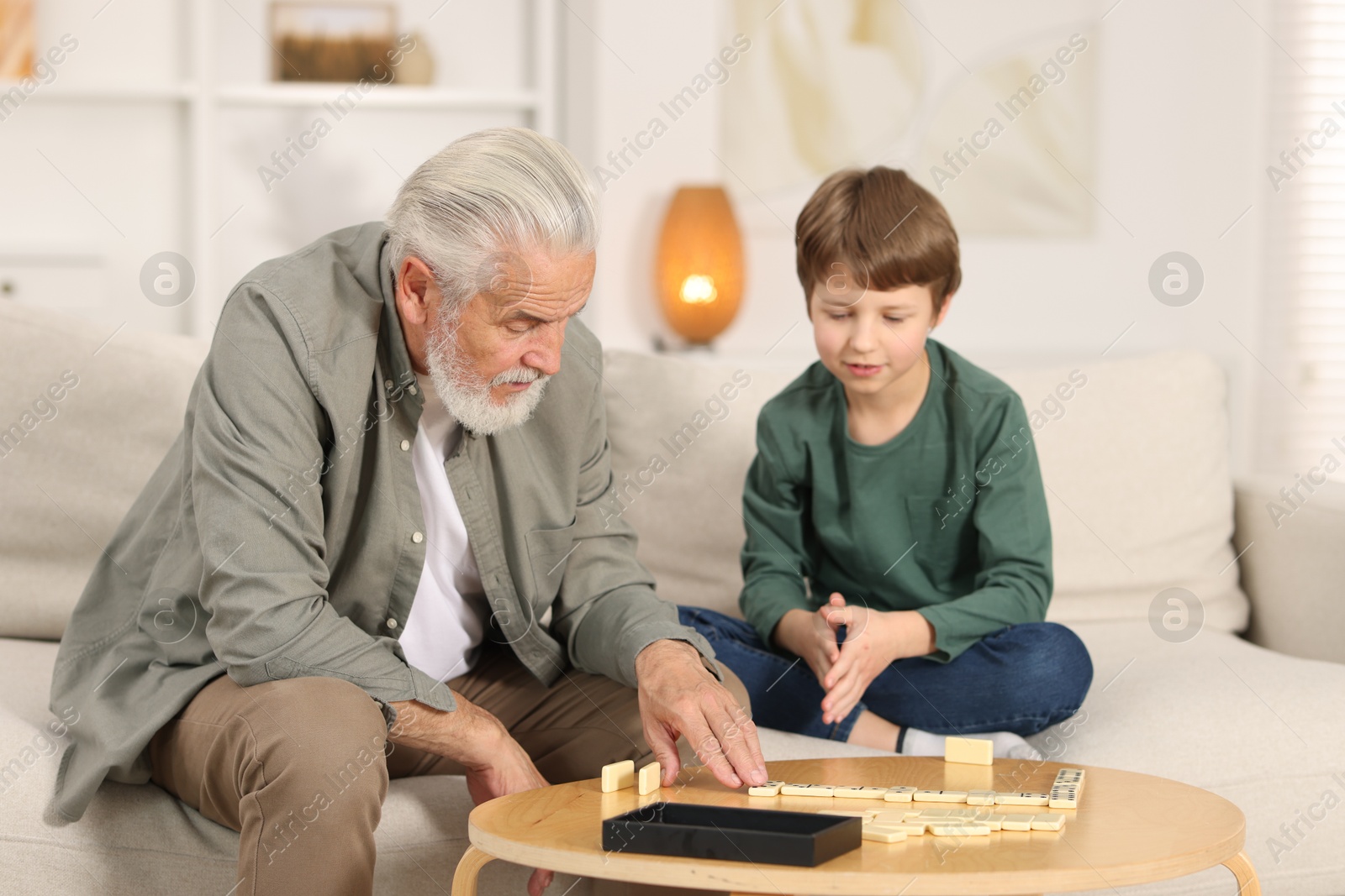 Photo of Grandpa and his grandson playing dominoes at table indoors