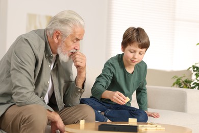 Grandpa and his grandson playing dominoes at table indoors