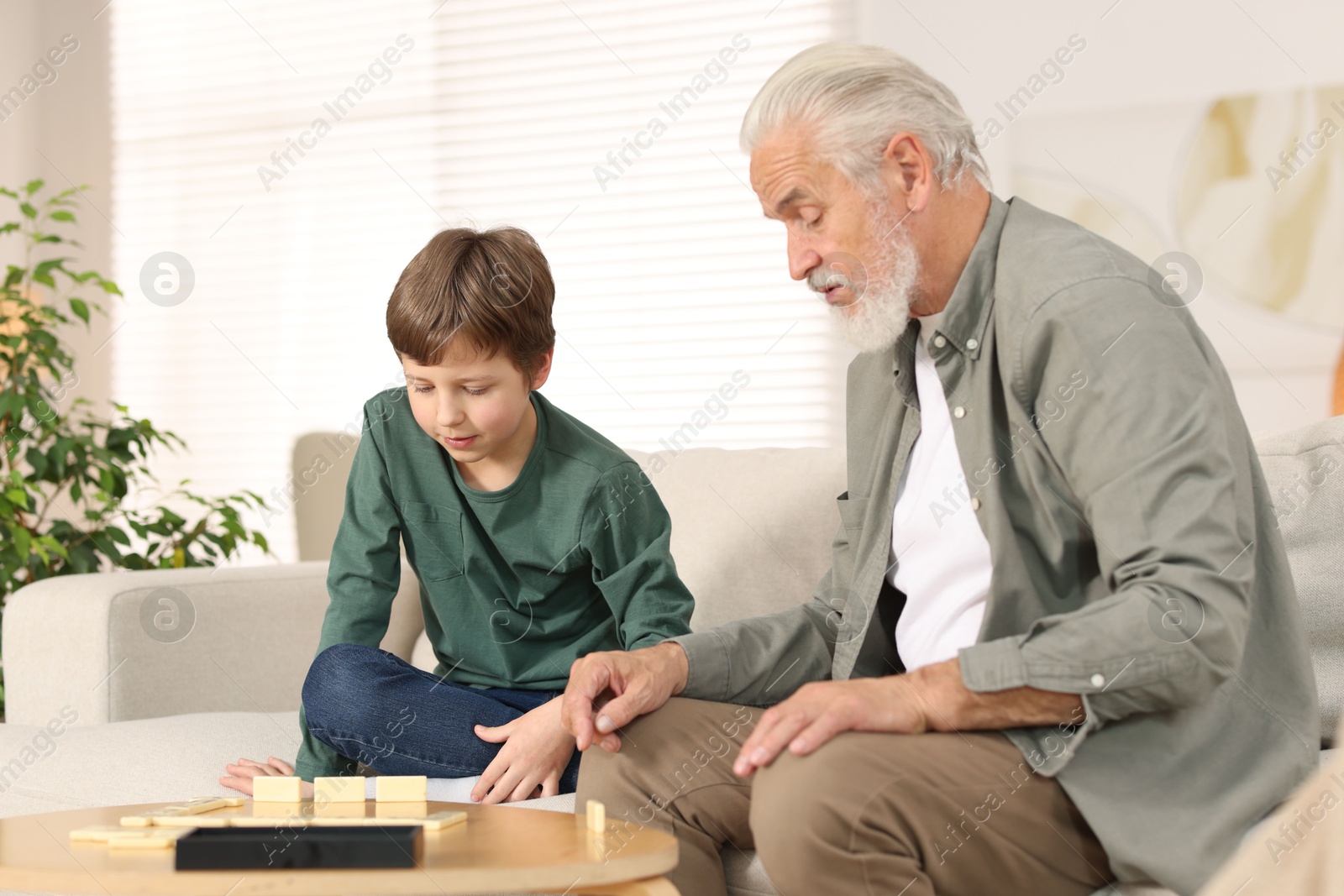 Photo of Grandpa and his grandson playing dominoes at table indoors