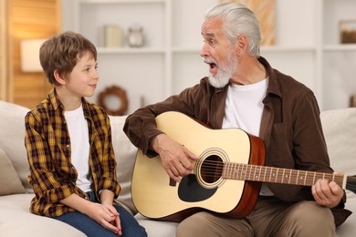 Grandpa teaching his grandson to play guitar on sofa at home