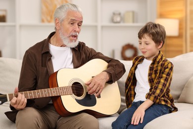 Photo of Grandpa teaching his grandson to play guitar on sofa at home