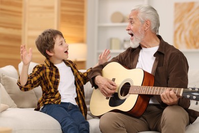 Grandpa teaching his grandson to play guitar on sofa at home