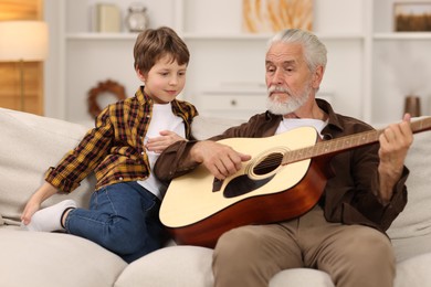 Grandpa teaching his grandson to play guitar on sofa at home