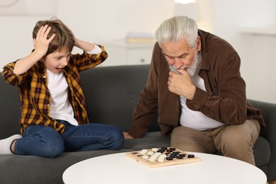 Photo of Grandpa and his grandson playing checkers at table indoors