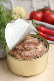 Photo of Canned meat in tin can on wooden table, closeup