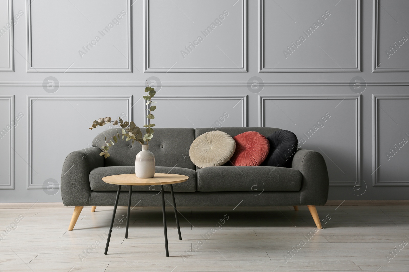 Photo of Stylish sofa with cushions and eucalyptus branches in vase on coffee table in room