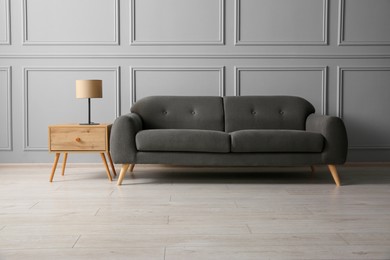 Photo of Stylish sofa and lamp on side table near grey wall