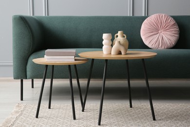 Photo of Stylish sofa with cushion, books and decor elements on nesting tables in room