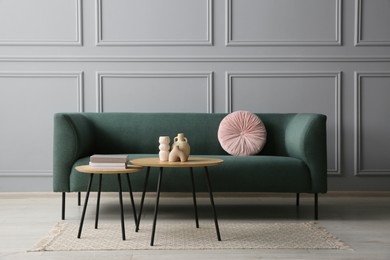 Photo of Stylish sofa with cushion, books and decor elements on nesting tables in room