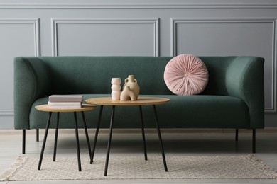 Photo of Stylish sofa with cushion, books and decor elements on nesting tables in room