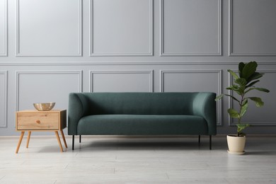 Photo of Stylish sofa, bowl on side table and green plant near grey wall