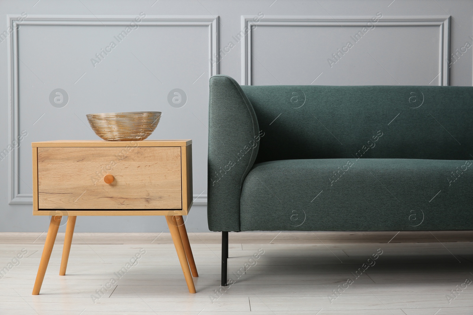 Photo of Stylish sofa and bowl on side table near grey wall