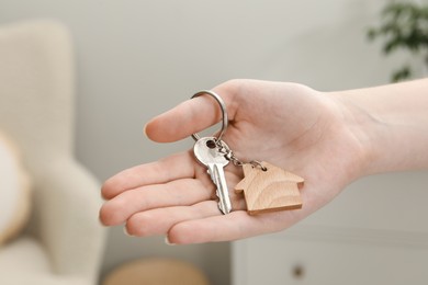 Photo of Woman holding key with house shaped keychain indoors, closeup