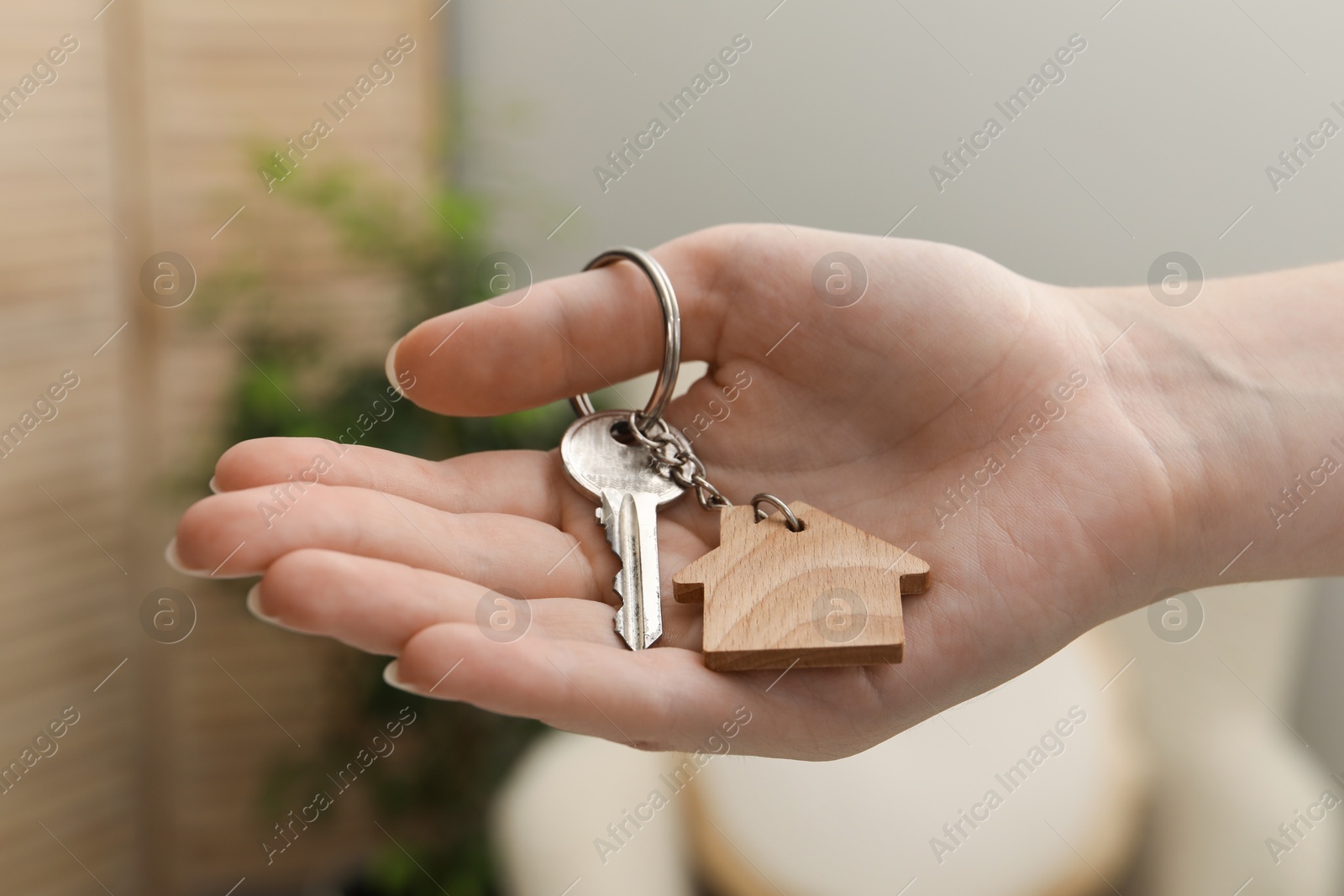 Photo of Woman holding key with house shaped keychain indoors, closeup