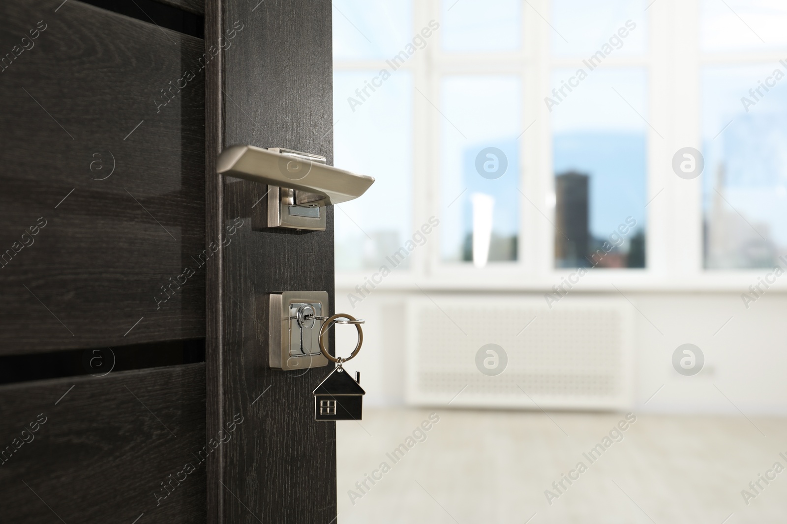 Photo of Open door with key and house shaped keychain, closeup. Space for text