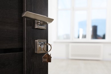 Photo of Open door with key and house shaped keychain, closeup. Space for text