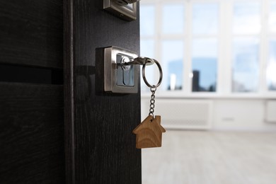 Photo of Open door with key and house shaped keychain, closeup. Space for text