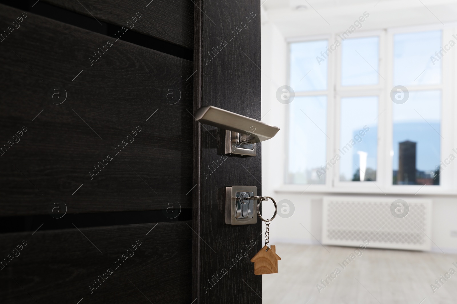 Photo of Open door with key and house shaped keychain, closeup. Space for text