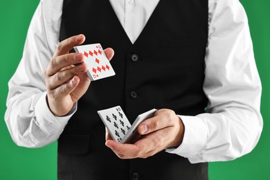 Photo of Professional croupier shuffling cards on green background, closeup