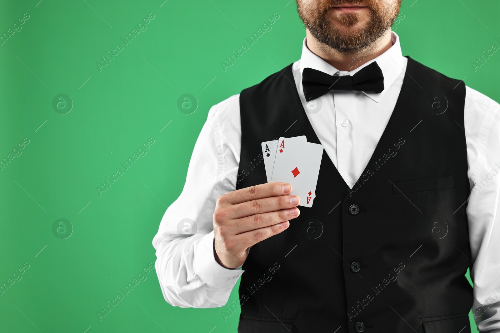 Photo of Professional croupier with playing cards on green background, closeup. Space for text