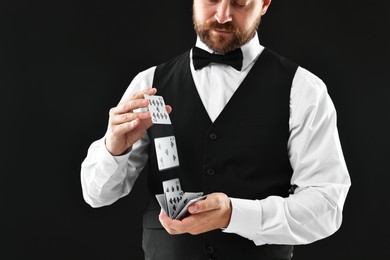 Professional croupier shuffling cards on black background, closeup