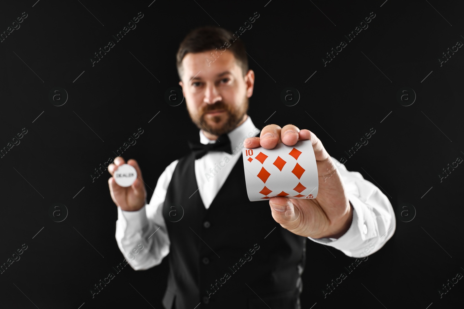 Photo of Croupier holding card and dealer button on black background, selective focus