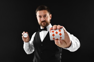 Croupier holding card and dealer button on black background, selective focus