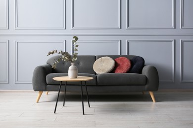 Photo of Stylish sofa with cushions and eucalyptus branches in vase on coffee table in room