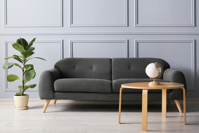 Photo of Stylish sofa, green plant and globe on coffee table in room