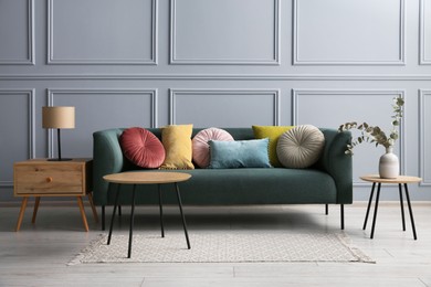 Photo of Stylish sofa with cushions, lamp and eucalyptus branches in vase on side tables in room