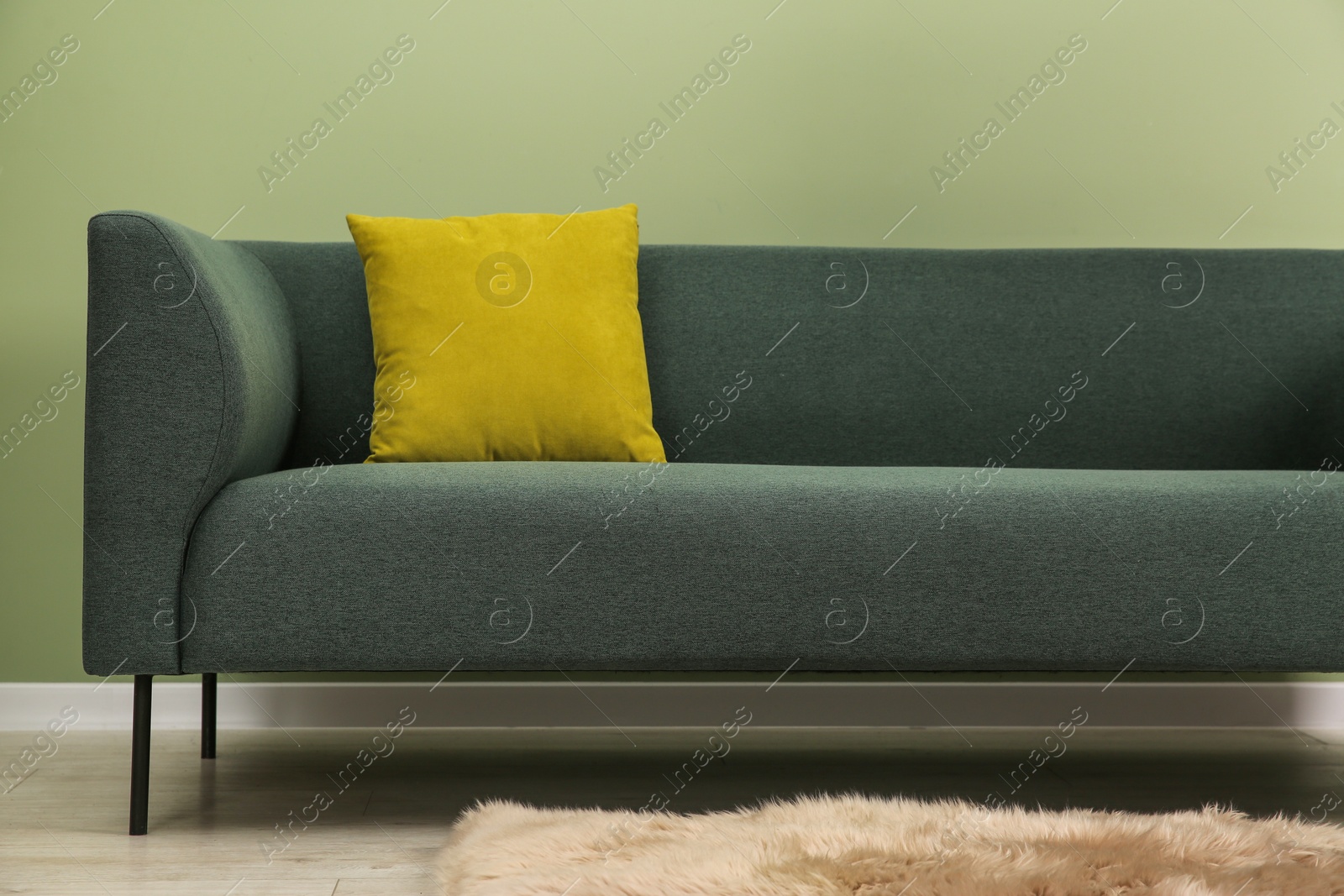 Photo of Stylish sofa with pillow near green wall indoors