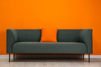 Photo of Stylish sofa with pillow near orange wall indoors